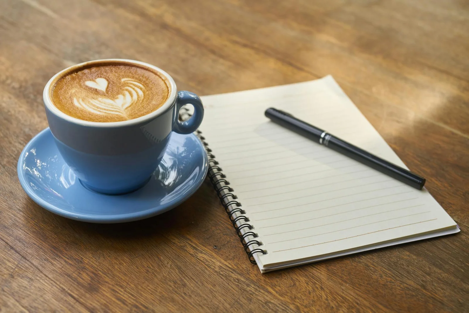 Closed notebook with pen on wooden desk, overhead view